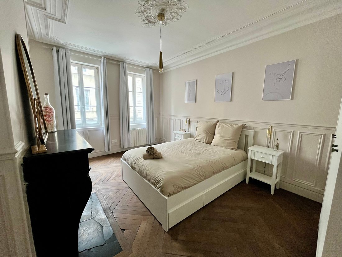 La même pièce après travaux : chambre en tons clairs, les mêmes boiseries repeintes, le même parquet point de Hongrie et la même cheminée en marbre noir, à gauche cette fois.