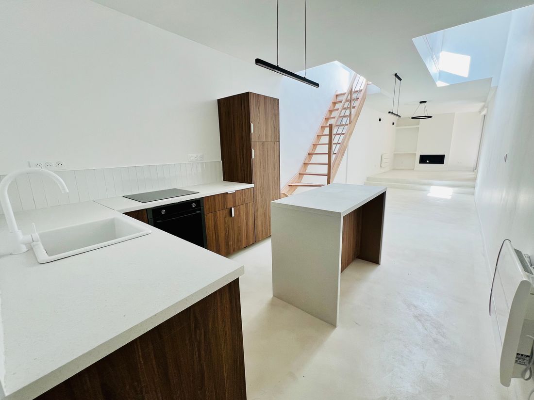 Les mêmes combles après travaux : loft avec cuisine ouverte, îlot central et sol en béton ciré.