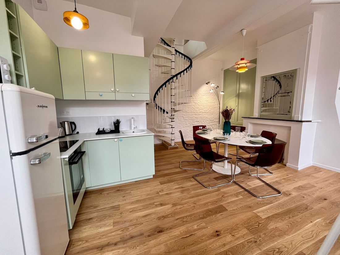Le même duplex après travaux : cuisine ouverte, parquet, et le même escalier en colimaçon repeint.