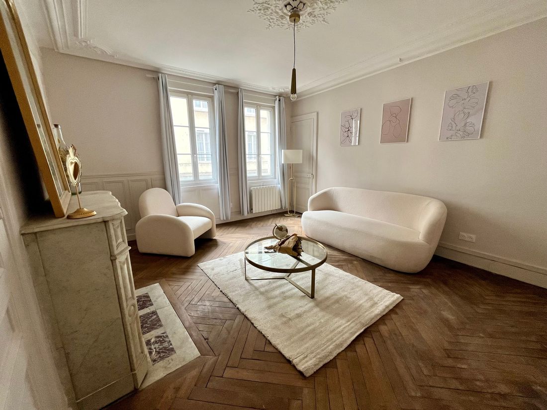 Le même salon après travaux : parquet point de Hongrie remis en état, murs clairs, la même cheminée en marbre et la même rosace.