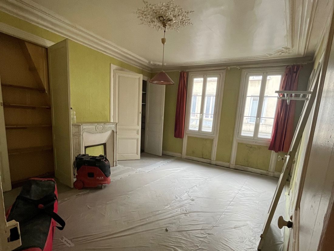 Le salon avant travaux : murs verts défraîchis, sol sous bâche, cheminée en marbre et rosace d'origine conservées.